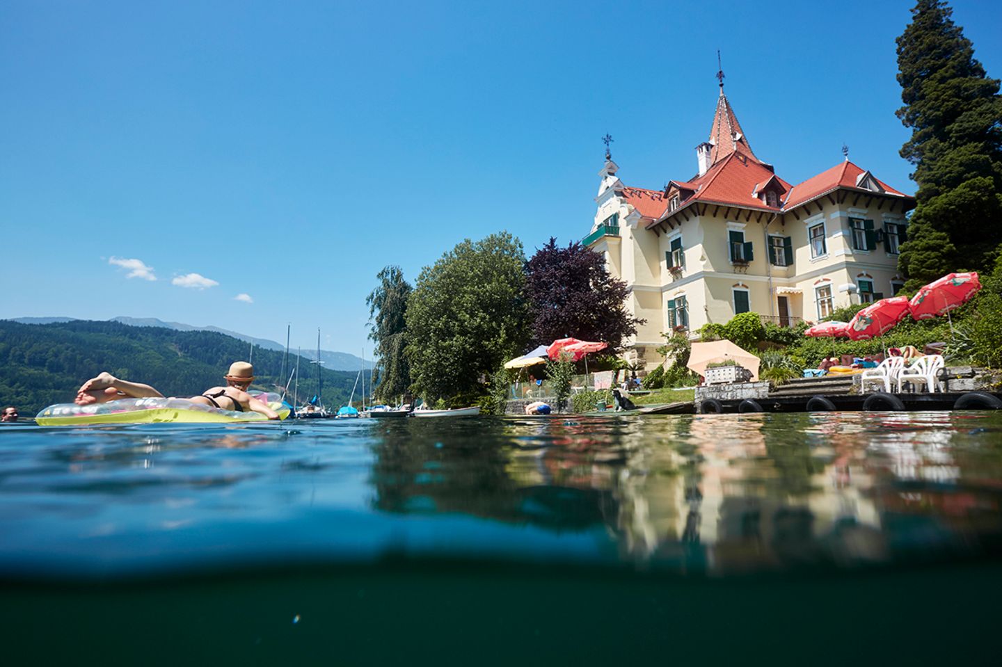Villa Verdin seen from the Millstätter See — turret, red roof, swimmers on the water